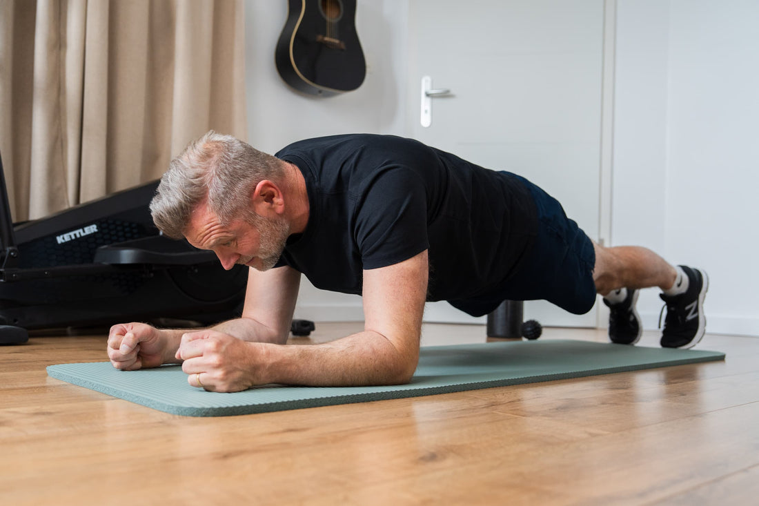 Homme d'une cinquantaine d'années en position de gainage sur tapis à domicile, illustrant un exercice de renforcement du corps fonctionnel adapté à la méthode Athlete40Plus après 40 ans.