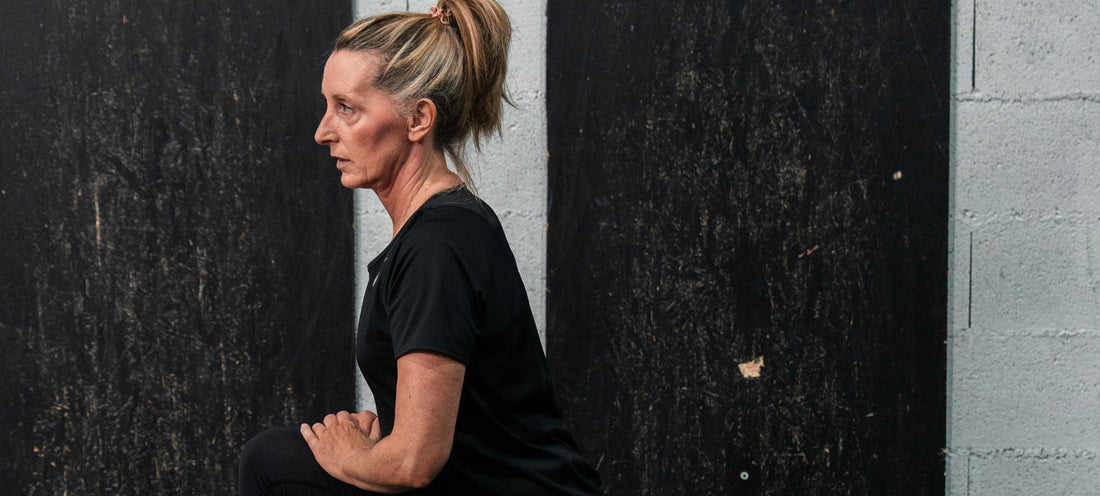 Femme d'une cinquantaine d'années effectuant un étirement du quadriceps debout contre un mur, illustrant la mobilité articulaire et la récupération active essentielles à la santé durable après 40 ans.