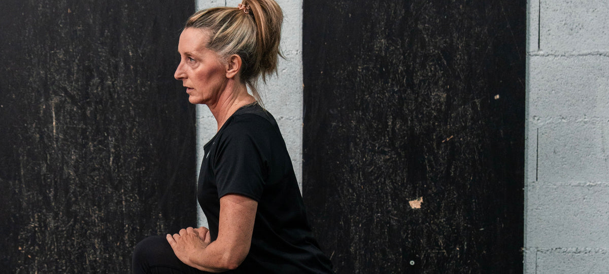 Femme d'une cinquantaine d'années effectuant un étirement du quadriceps debout contre un mur, illustrant la mobilité articulaire et la récupération active essentielles à la santé durable après 40 ans.